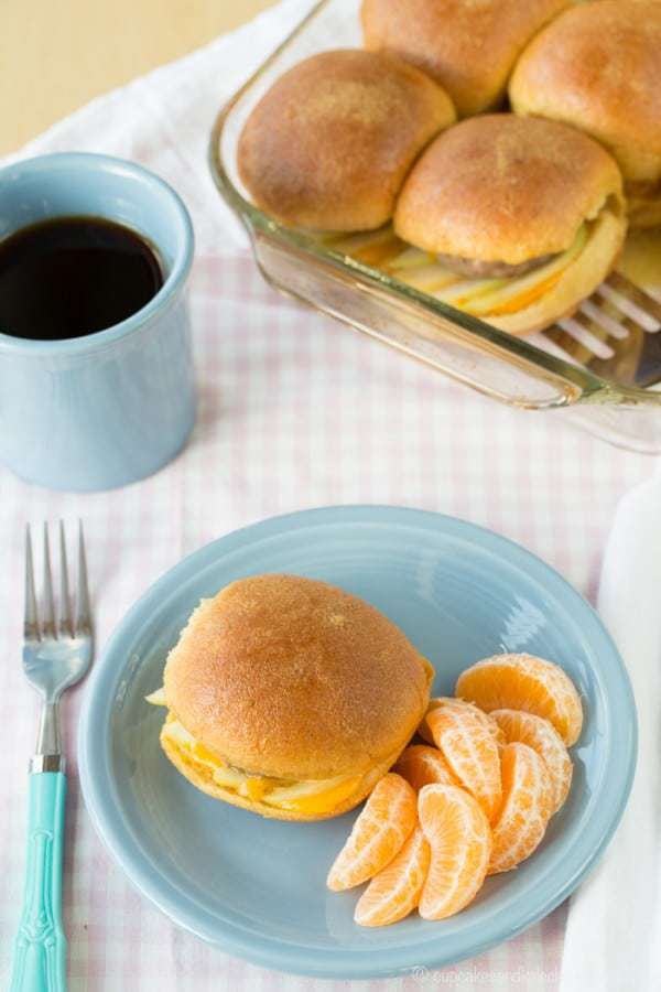 An apple turkey sausage slider on a plate with clementine wedges, next to a cup of coffee.