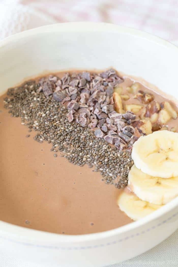 Chocolate smoothie bowl topped with walnuts, cacao nubs, chia seeds, and banana slices