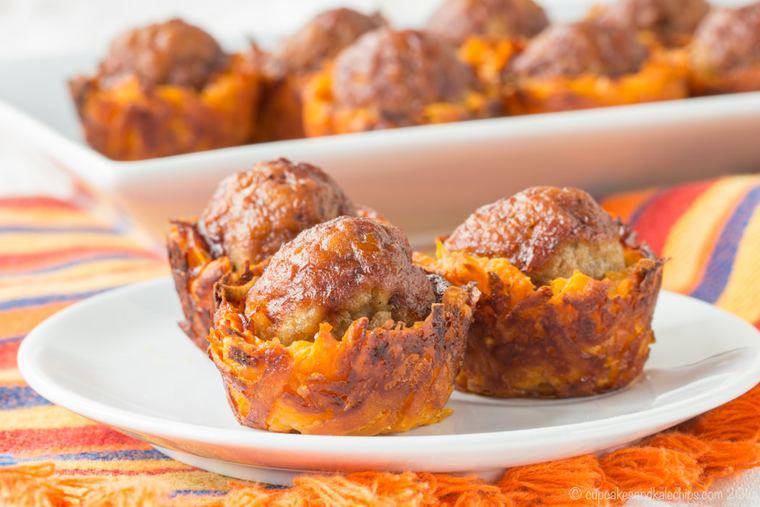 Three meatballs in sweet potato cups on a plate with more in the background on a platter.