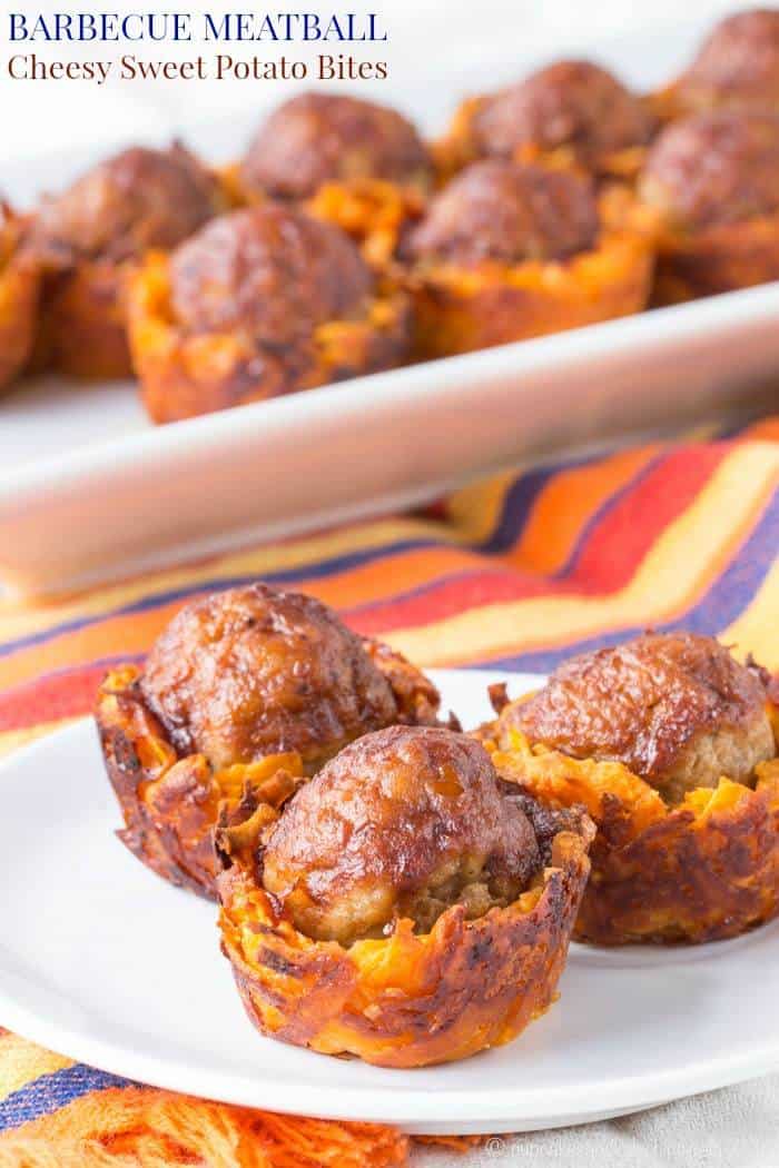 Three meatballs in sweet potato cups on a plate with more in the background on a platter.