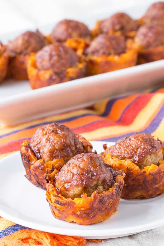 Three meatballs in sweet potato cups on a plate with more in the background on a platter.
