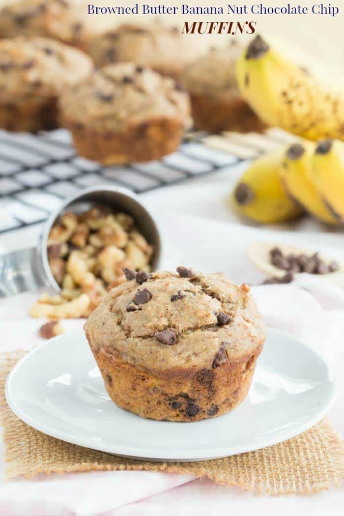 A browned butter banana chocolate chip muffin on a white plate, with muffins and bananas in the background.