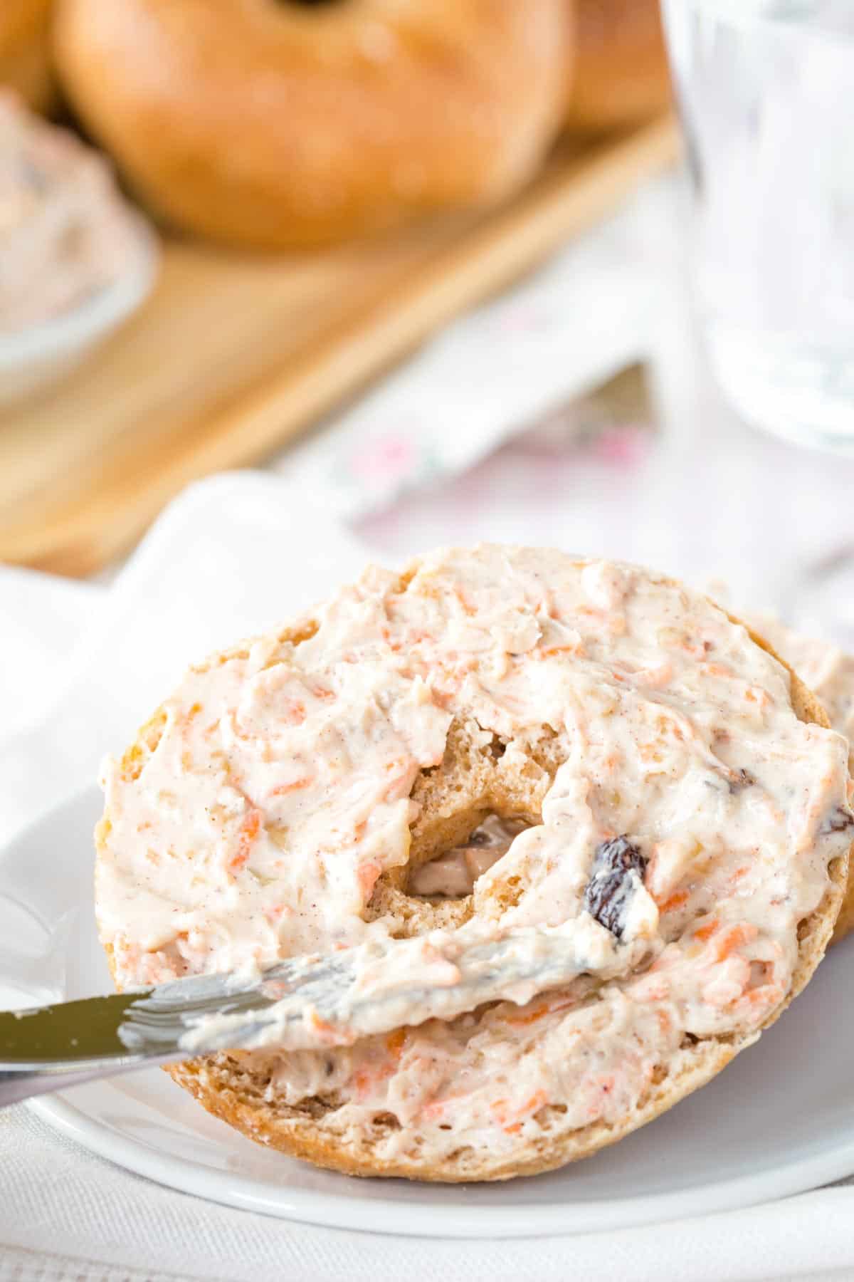 Carrot Cake Whipped Cream Cheese being spread on a bagel with a small knife.