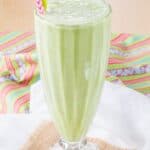 A green smoothie in a milkshake glass with two straws on top of colorful napkins with text overlay that says "Healthy Shamrock Shake Mint Smoothie".