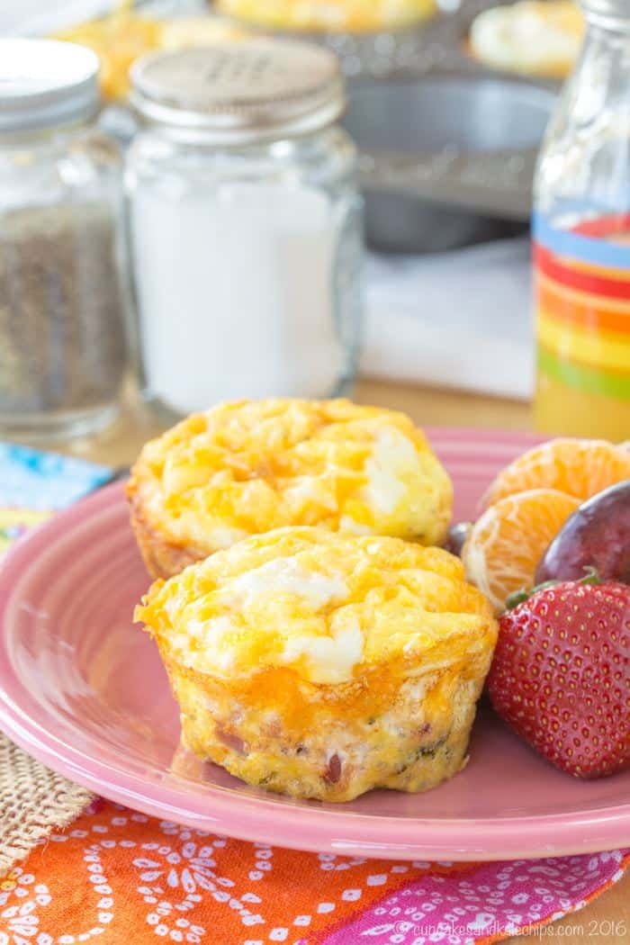 Two broccoli, ham and cheese egg muffins on a plate next to fruits.