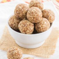 Pineapple coconut energy balls in a small white bowl on a piece of burlap and two more on a cloth napkin