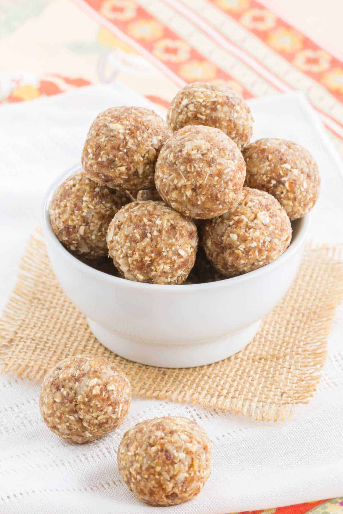 Pineapple coconut energy balls in a small white bowl on a piece of burlap and two more on a cloth napkin