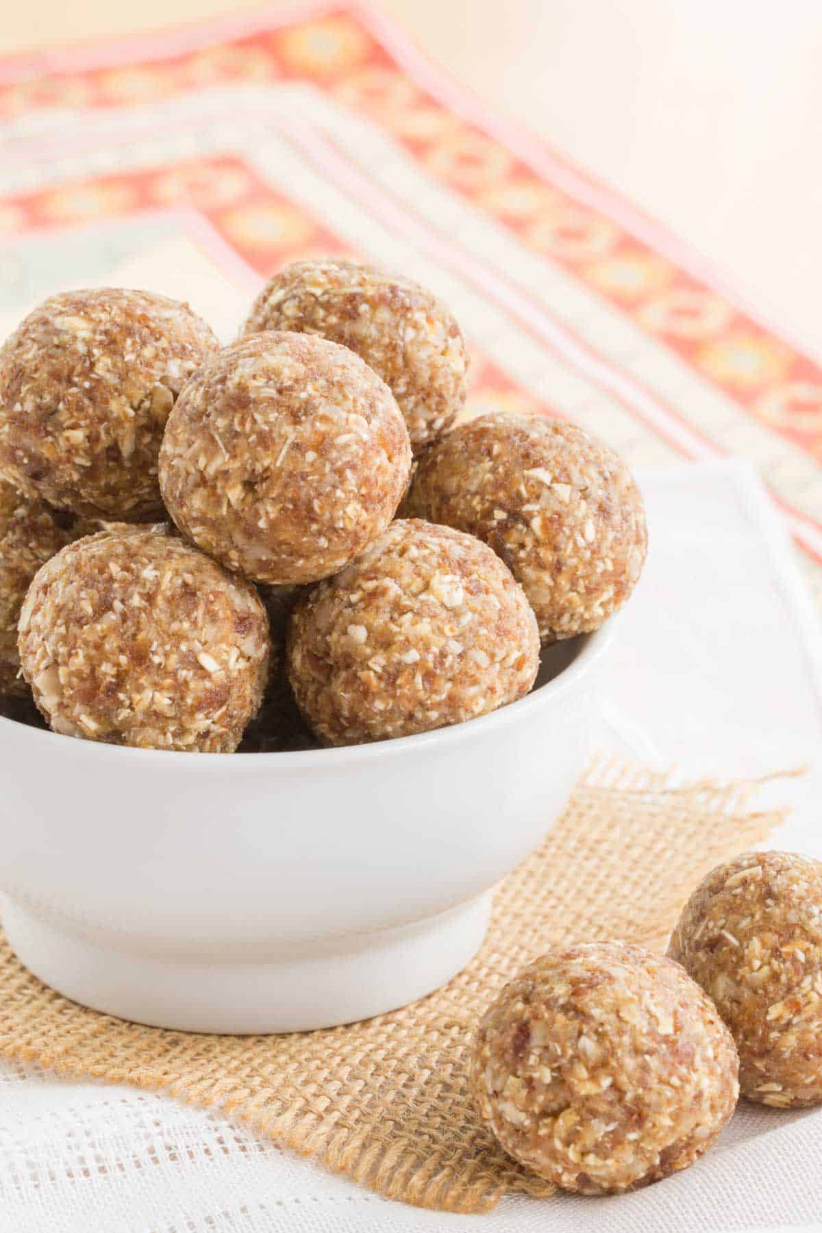 pineapple coconut energy balls in a white bowl with two on a piece of burlap on top of a cloth napkin