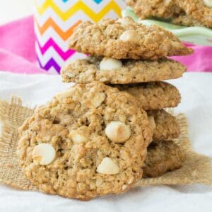 A gluten free white chocolate chip oatmeal cookie leaning against stacked cookies.
