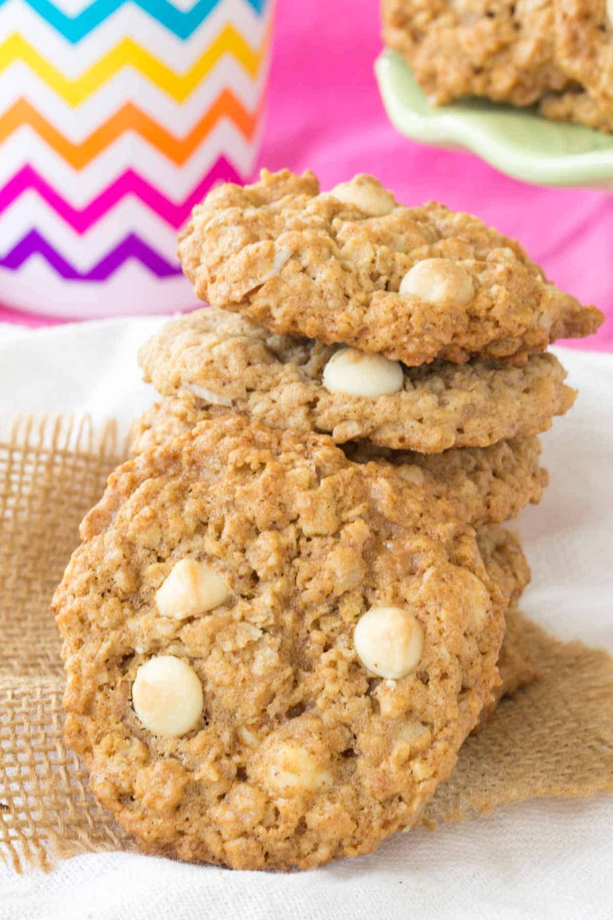 A stack of White Chocolate Chip Oatmeal Cookie with one leaning against the stack on top of a piece of burlap.
