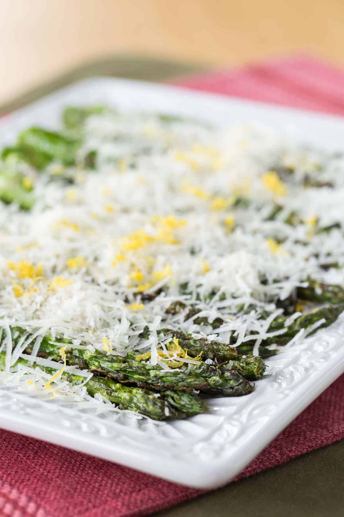 Grilled Asparagus with Lemon and Manchego cheese on a white rectangular plate
