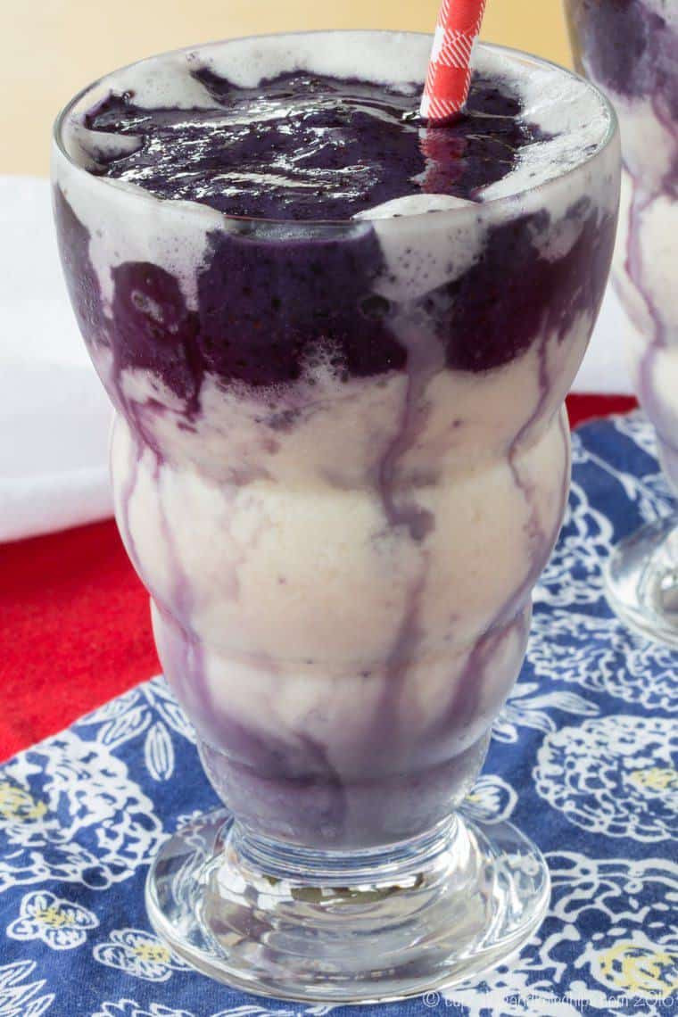 A blueberry smoothie in a tall glass with a red and white striped straw.