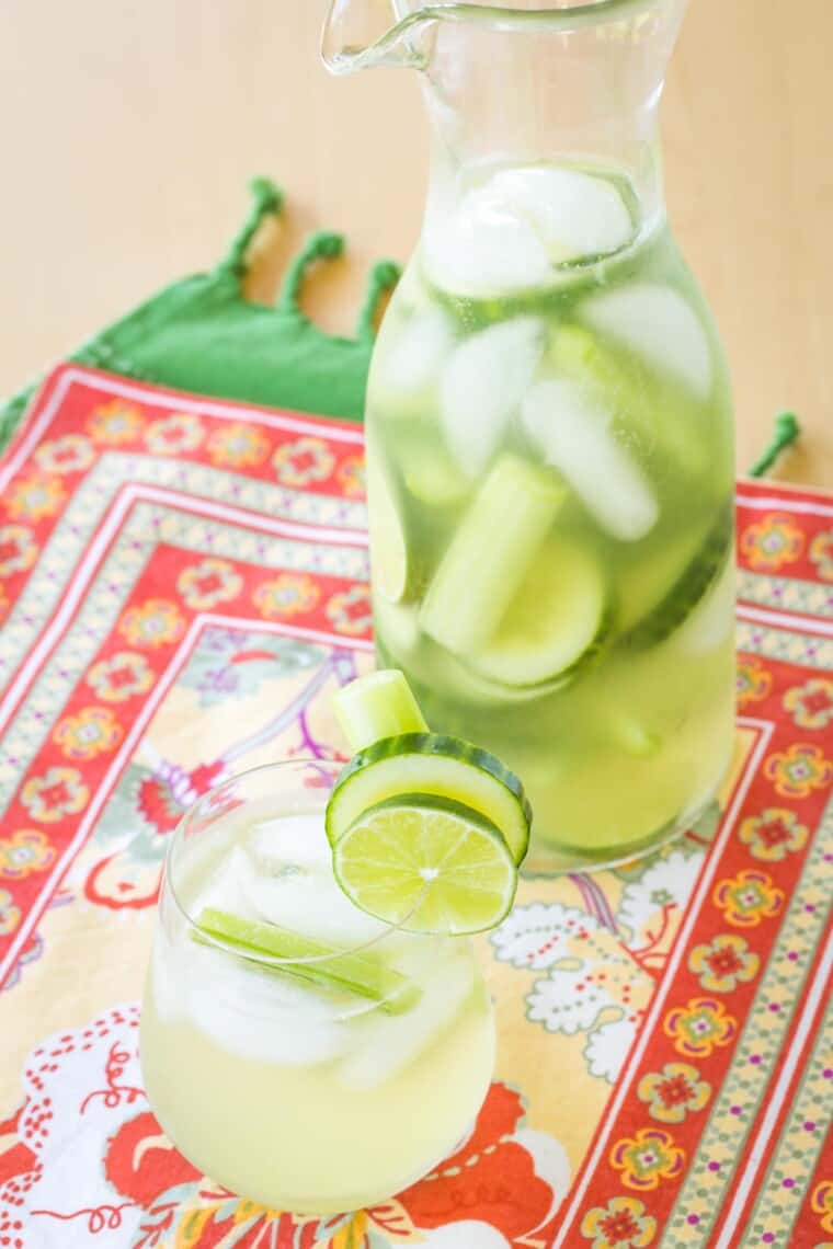 clear pitcher and a stemless wine glass filled with cucumber gimlet white sangria garnished with cucumber and lime slices and celery