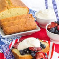 A sliced loaf of pound cake with one slice on a plate topped with mixed berries.