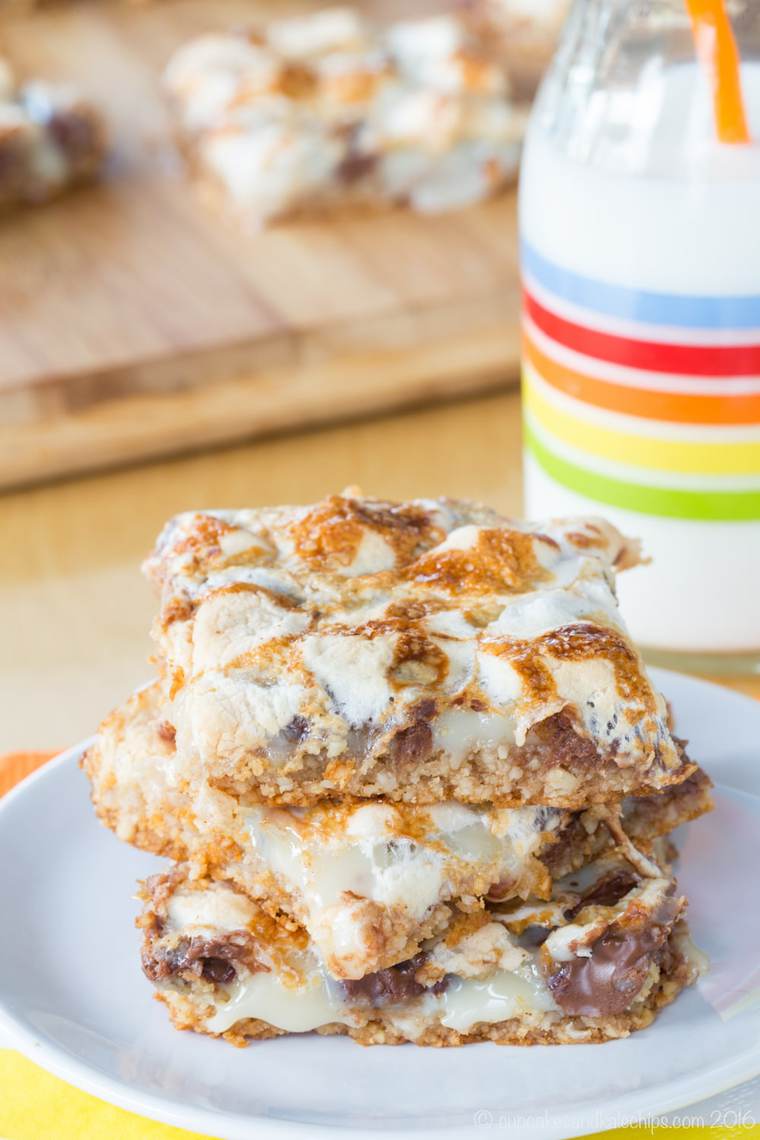 Three s'mores bars stacked on a plate with a glass of milk in the background.