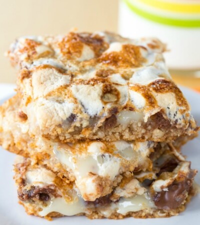 Three s'mores bars stacked on a plate with a glass of milk in the background.