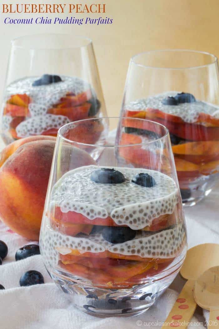 Blueberry and Peach Chia Pudding Parfaits in glasses, next to a whole peach and scattered blueberries.