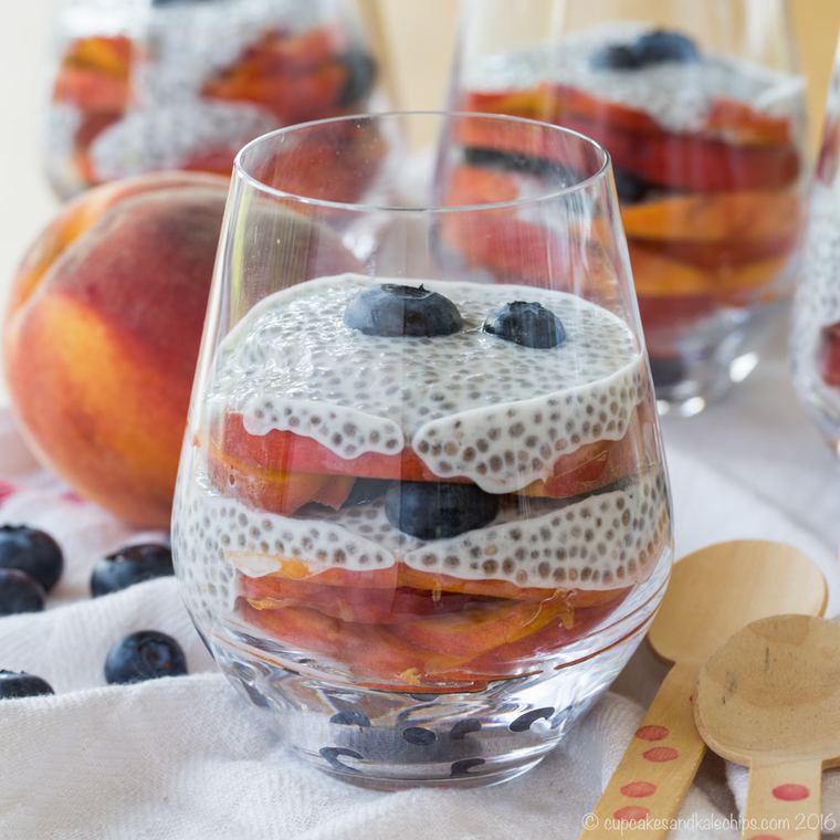 Blueberry and Peach Chia Pudding Parfaits in glasses, next to a whole peach and scattered blueberries.