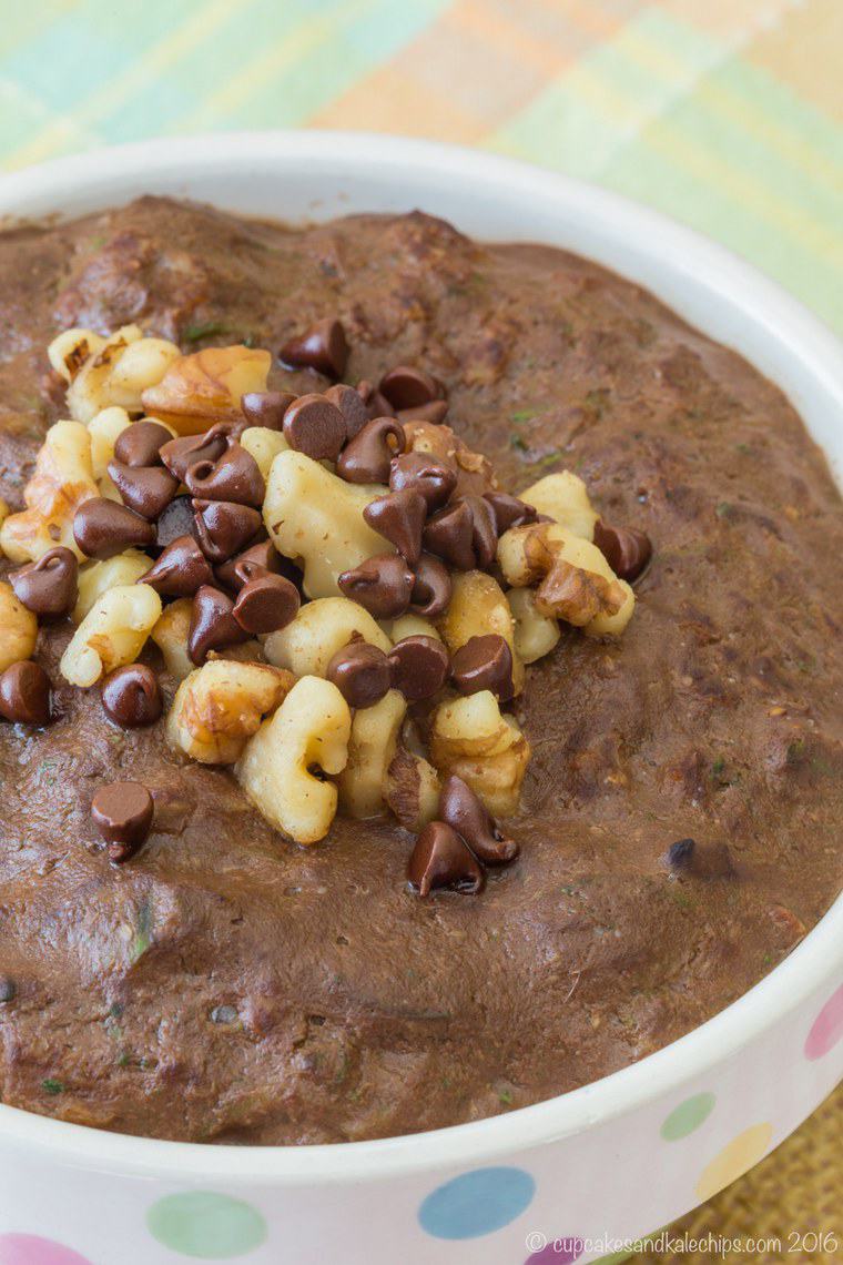 Close up of a bowl of zucchini oatmeal stopped with crushed nuts and chocolate chips.