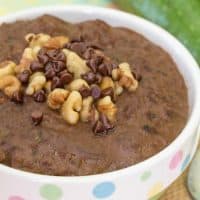 A bowl of zucchini oatmeal stopped with crushed nuts and chocolate chips.