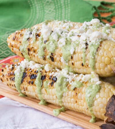 A wooden platter of Peruvian street corn on top of a colorful placemat and a white cloth napkin.