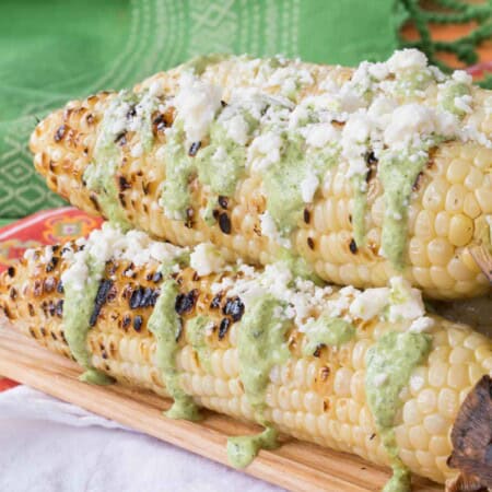 A wooden platter of Peruvian street corn on top of a colorful placemat and a white cloth napkin.