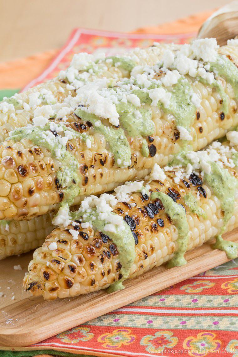 Three ears of grilled corn drizzled with green aji sauce and sprinkled with cheese.