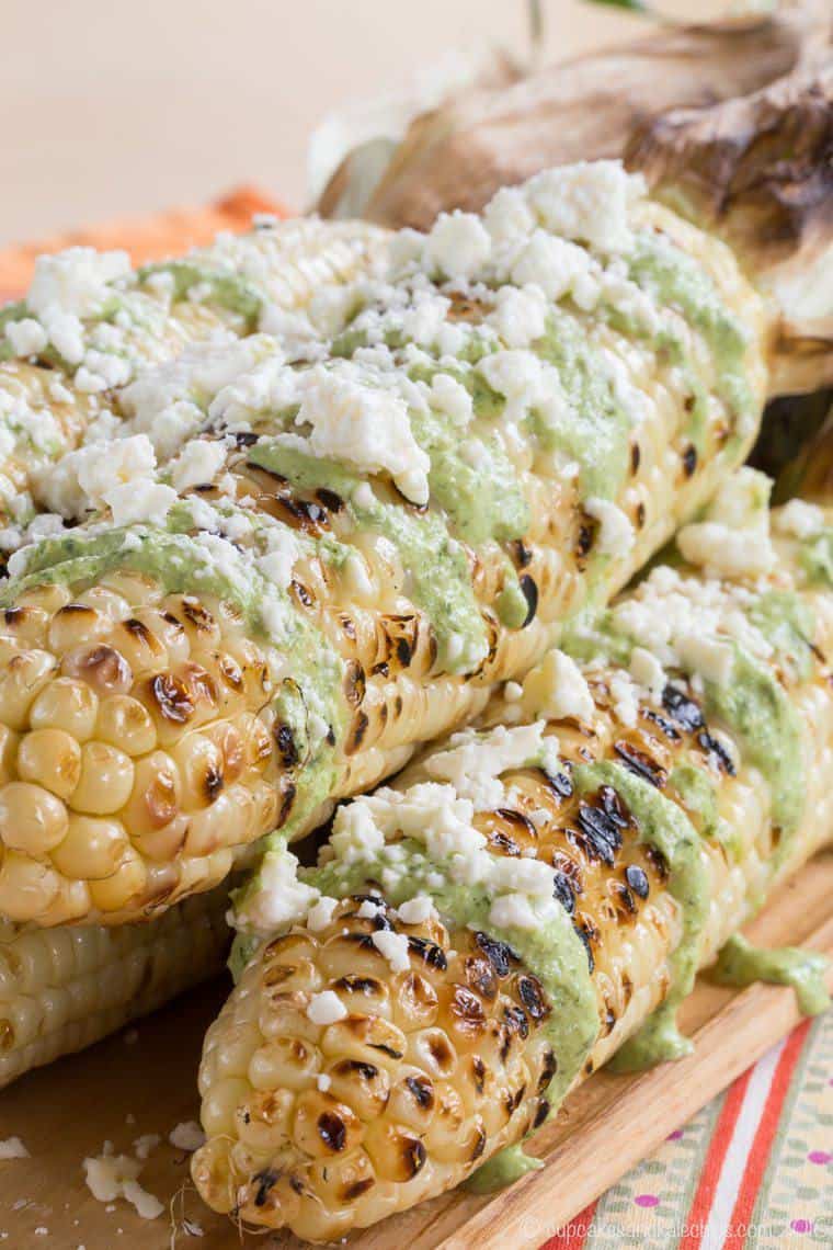 A closeup of Peruvian Corn on the cob which is grilled ears of corn topped with a drizzle of aji sauce and crumbled cotija cheese.