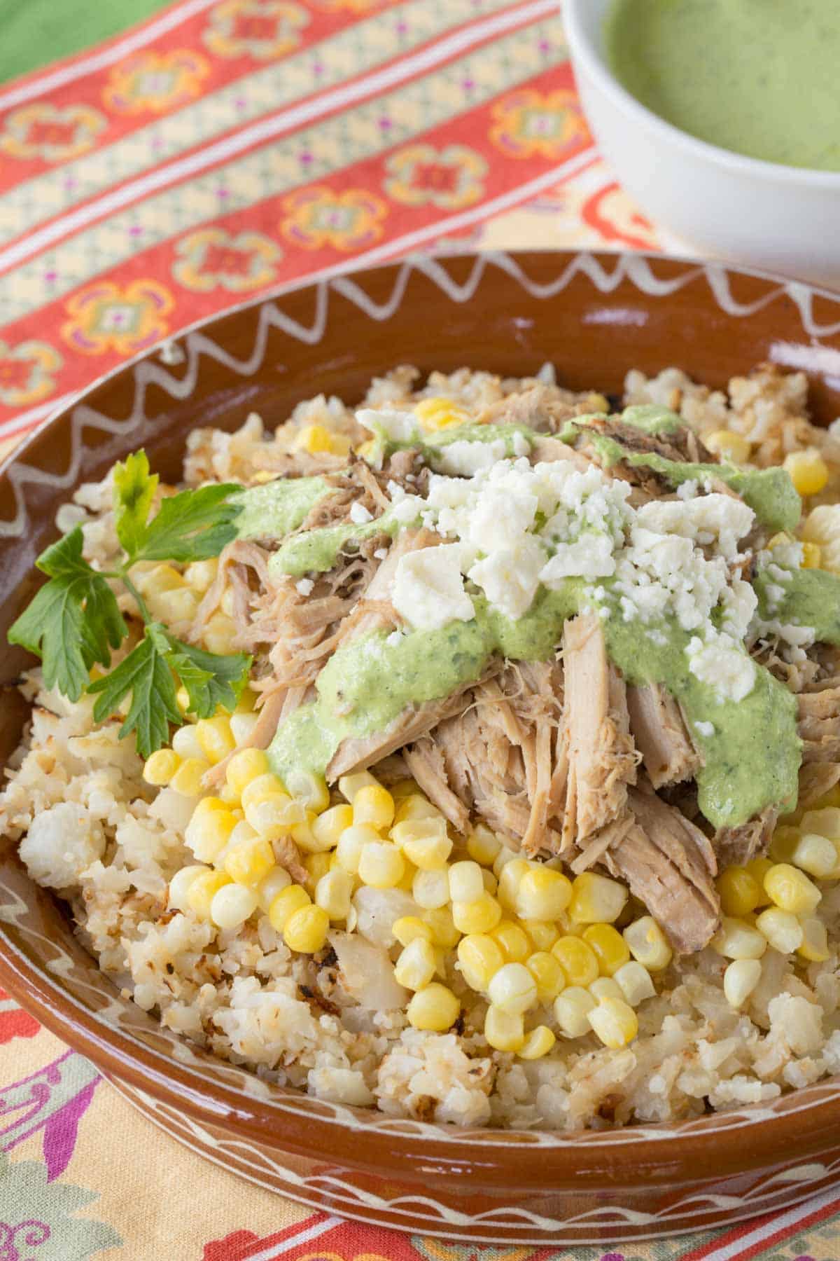 Slow Cooker Peruvian Pulled Pork served over cauliflower rice with corn, a drizzle of aji sauce, and crumbled queso fresco.