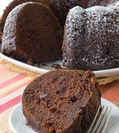 A slice of gluten free chocolate pumpkin cake on a plate with the rest of the cake behind it.