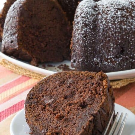 A slice of gluten free chocolate pumpkin cake on a plate with the rest of the cake behind it.