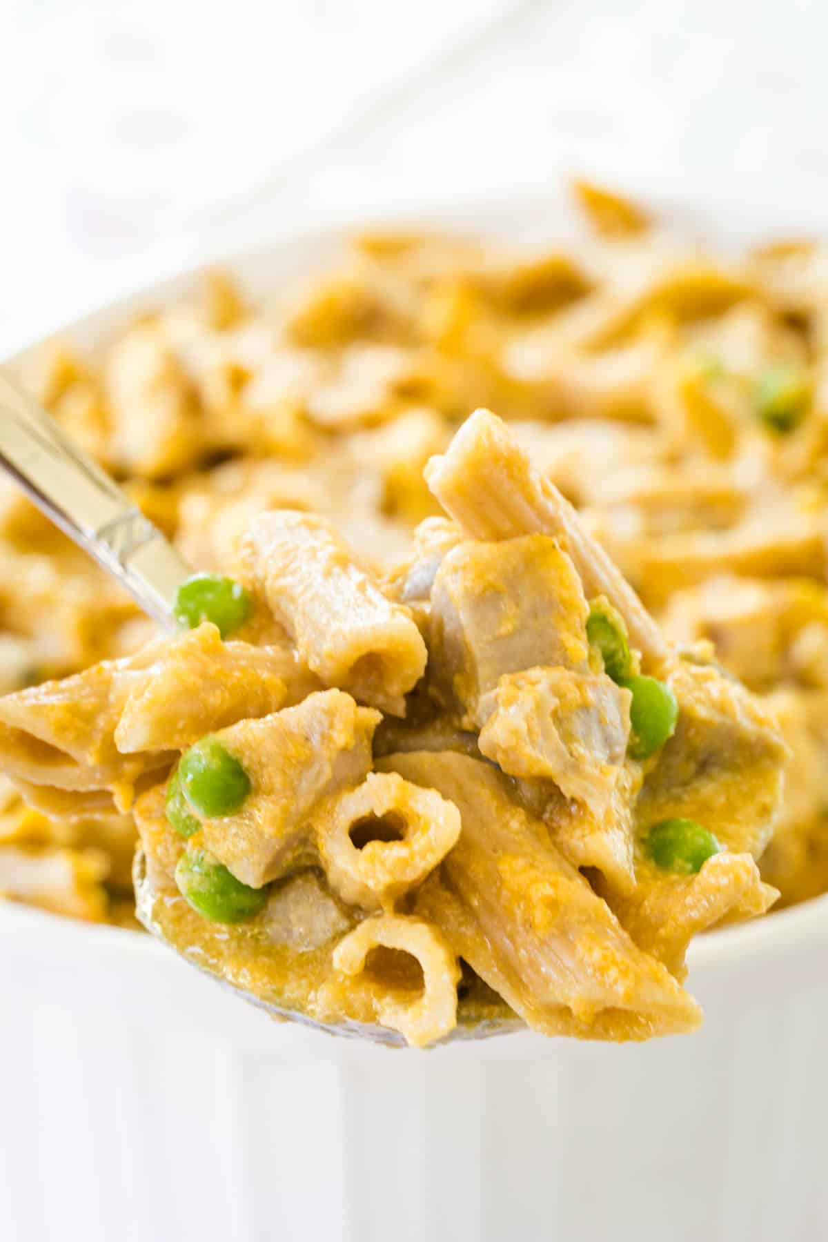 A forkful of baked penne paste in pumpkin cream sauce in the foreground with the casserole dish in the background.