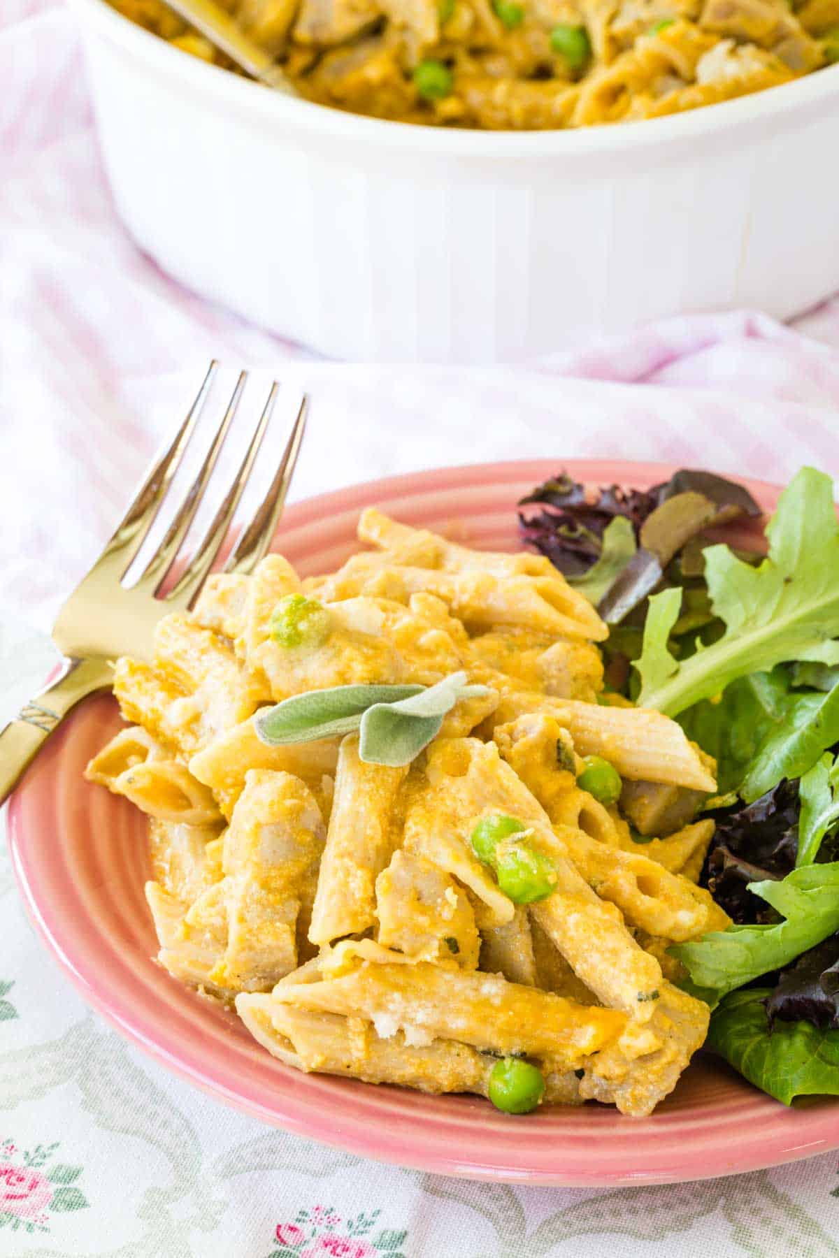 A plate of creamy baked penne casserole on a plate next to a side of green salad.