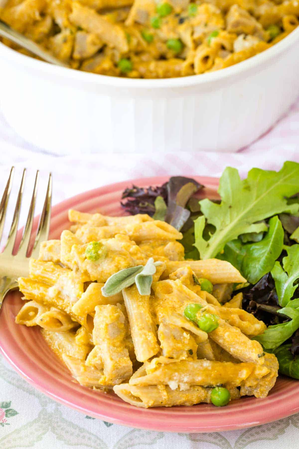 Pumpkin penne with cream sauce is served with a side of green salad, next to a fork.