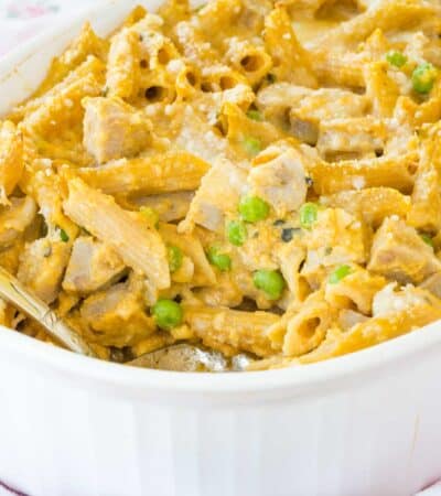 Creamy pumpkin penne with chicken sausage is spooned from a baking dish.