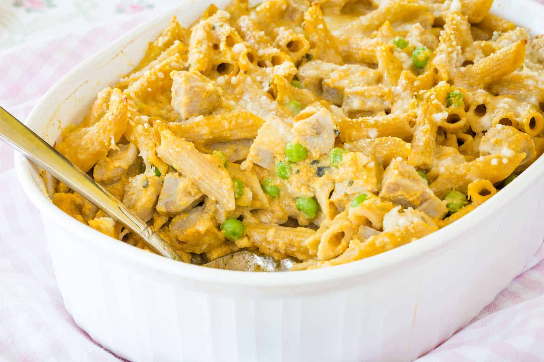 Creamy pumpkin penne with chicken sausage is spooned from a baking dish.
