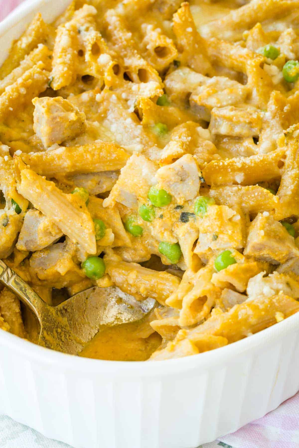 Creamy pumpkin penne with chicken sausage is spooned from a baking dish.