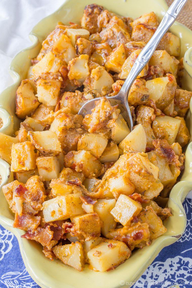 Cheddar Bacon Ranch Roasted Potatoes in a yellow oval serving dish with a spoon