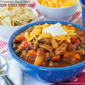 Slow Cooker Turkey Chili topped with shredded cheese and sour cream in a blue bowl, with bowls of toppings in the background.