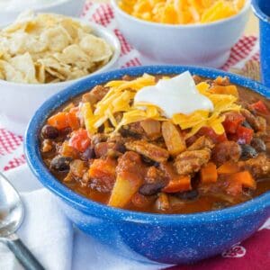 Slow Cooker Turkey Chili topped with shredded cheese and sour cream in a blue bowl, with bowls of toppings in the background.