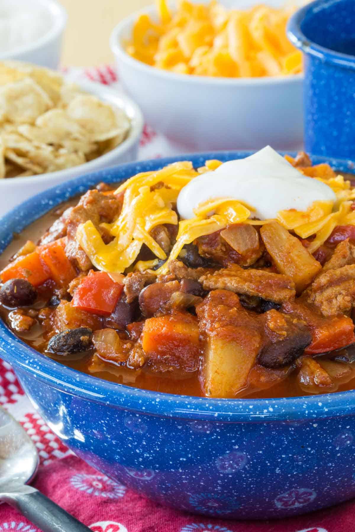 Slow Cooker Turkey Chili topped with shredded cheese and sour cream in a blue bowl, with bowls of toppings in the background.