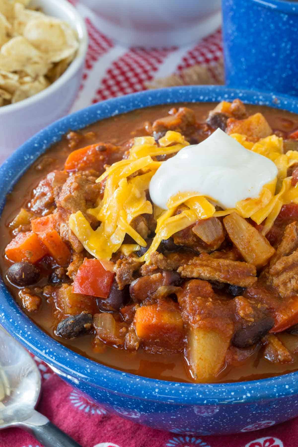 Close up of Slow Cooker Turkey Chili topped with shredded cheese and sour cream in a blue bowl.