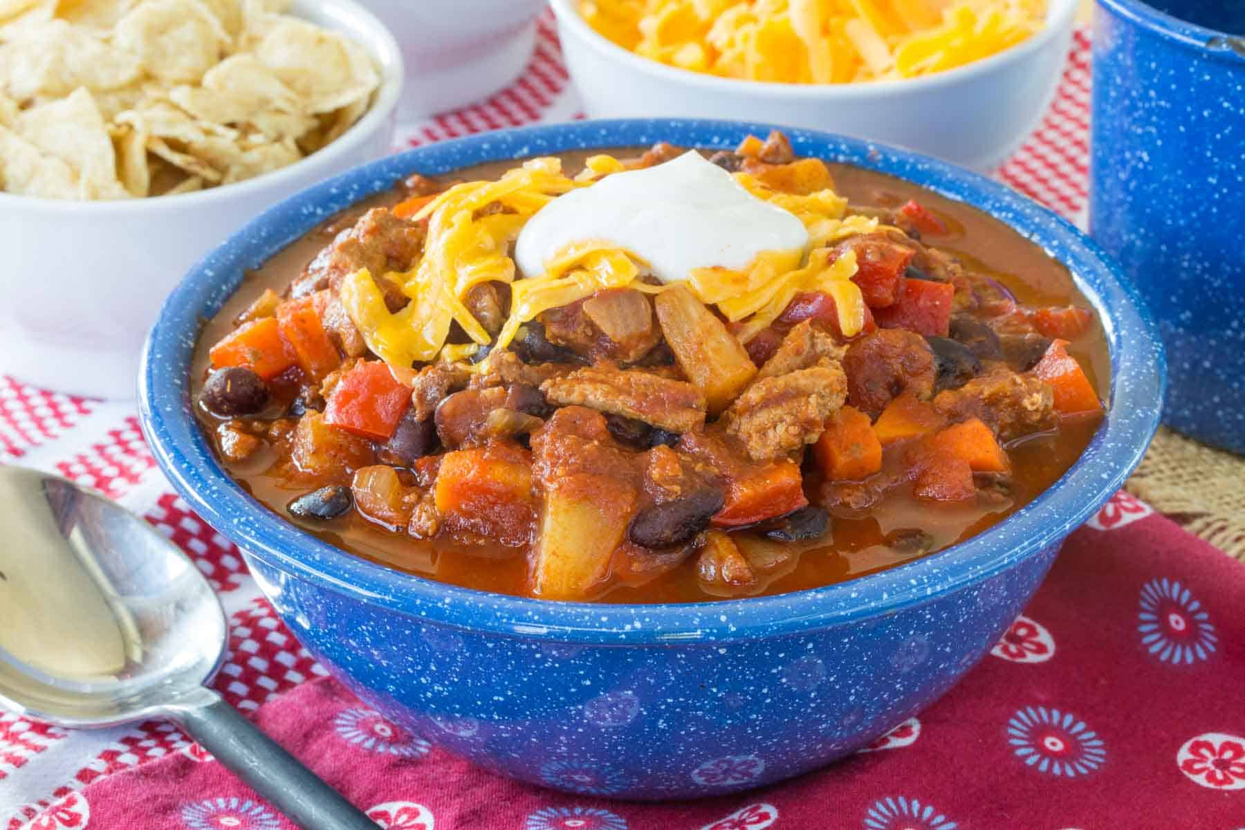 Slow Cooker Turkey Chili topped with shredded cheese and sour cream in a blue bowl, with bowls of toppings in the background.