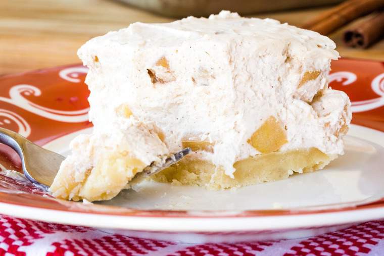 A square slice of apple cinnamon no-bake cheesecake bars with a bite on a fork