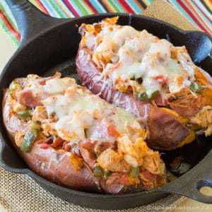 Two baked sweet potatoes with jambalaya stuffing and melted cheese in a cast iron skillet.