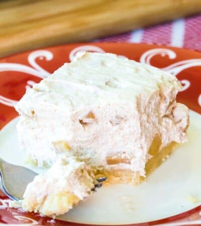 A apple cheeswecake bar on a plate with one bite on a fork.