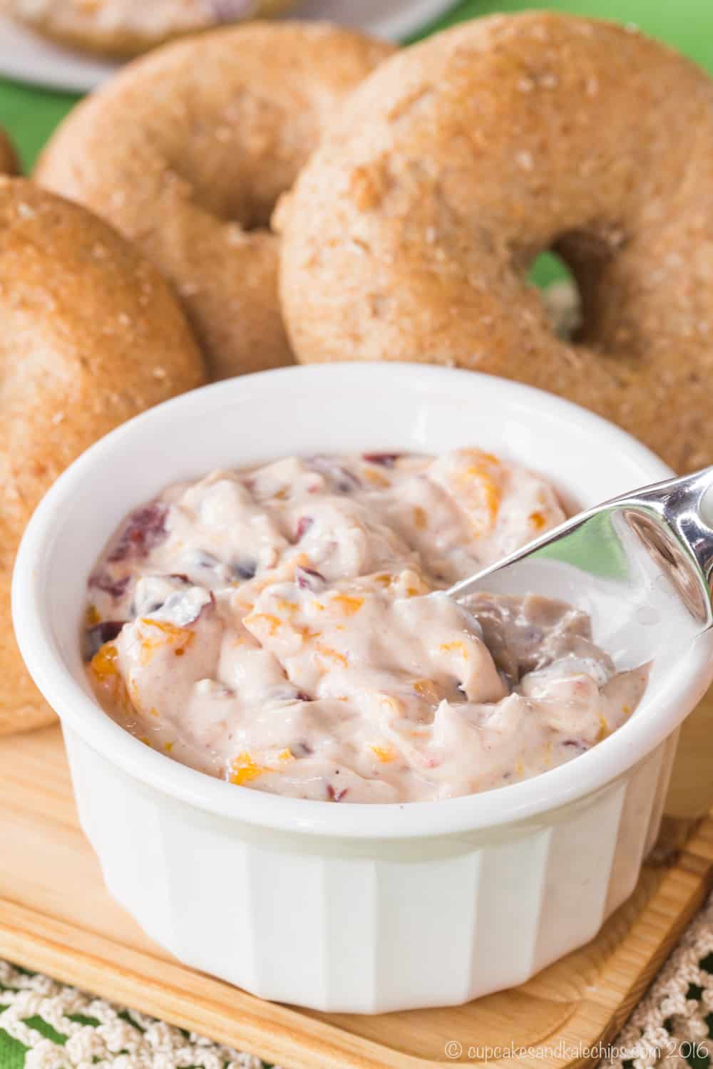 A small white crock filled with Cranberry Orange Cream Cheese on a wooden platter with a small spreader knife in it.