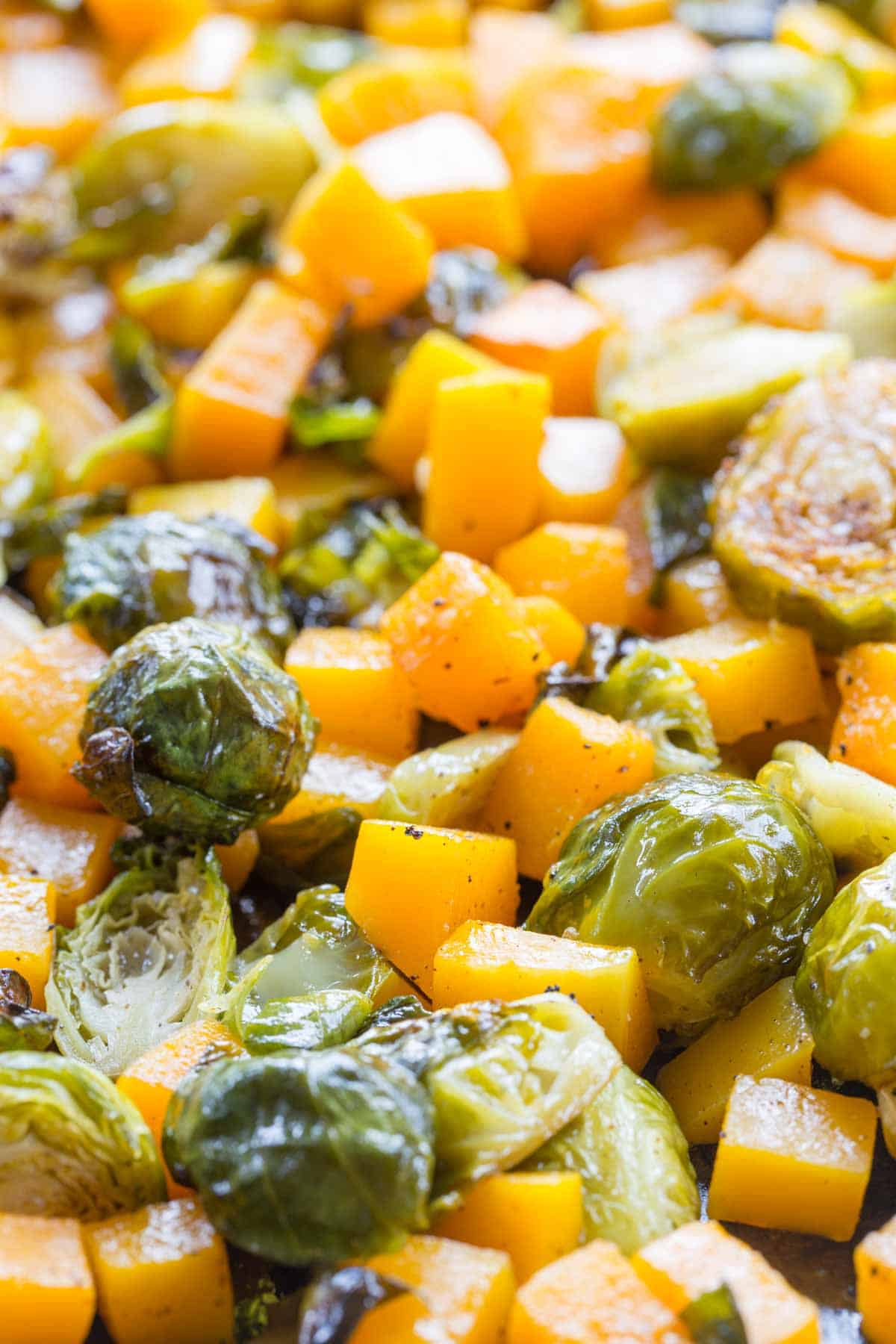 A mixture of squash cubed and Brussel sprouts roasted on a baking sheet.