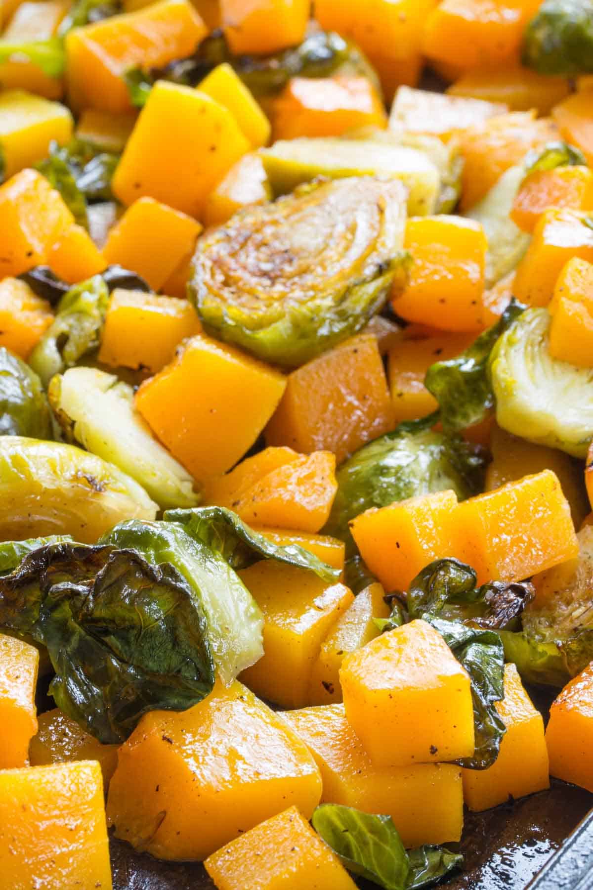 Roasted halved Brussels sprouts mixed with cubes of butternut squash on a sheet pan.