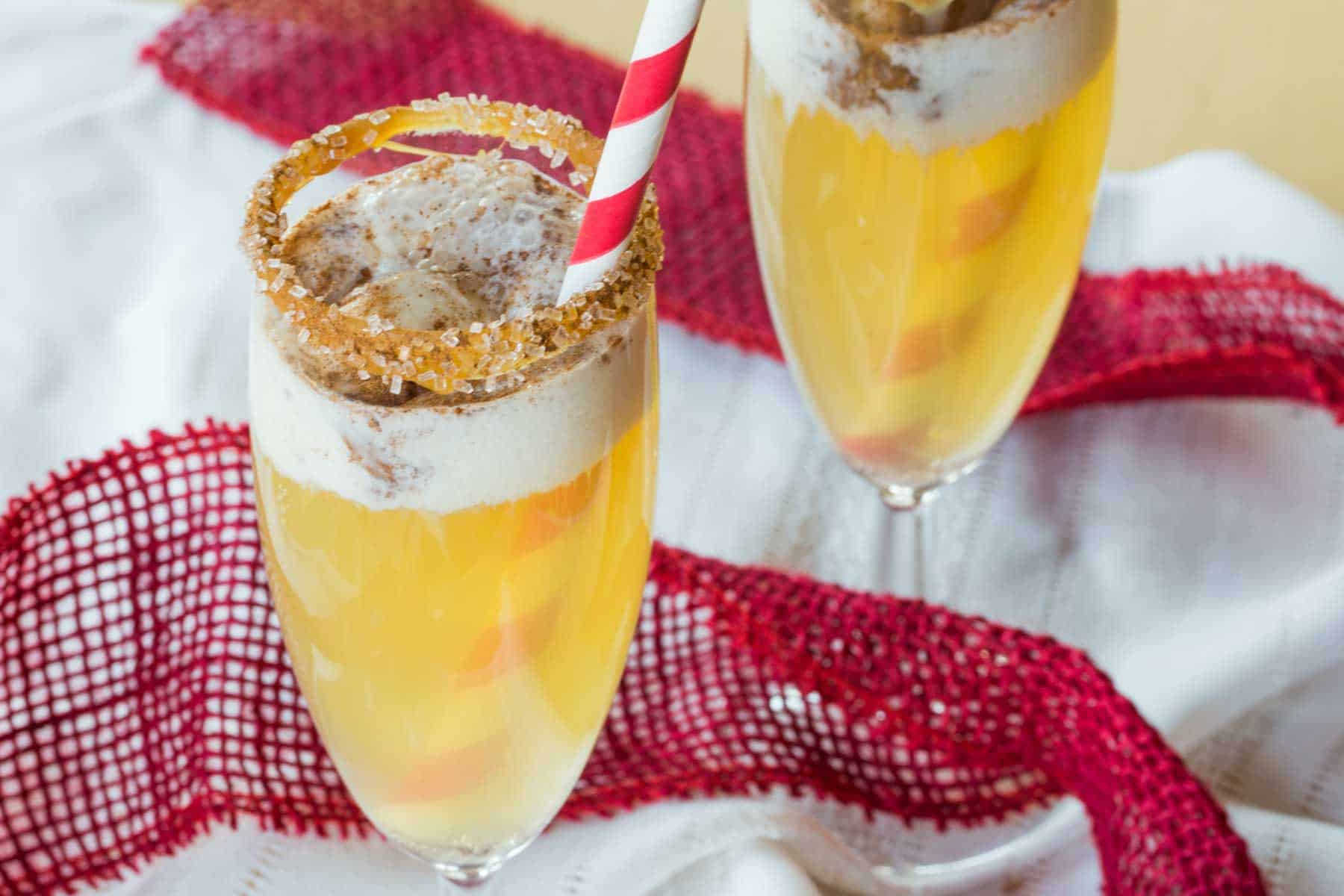 A champagne flute of sparkling cider with a scoop of vanilla ice cream in it with a cinnamon-sugar rim.